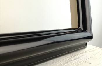 Profiled moulding of a black high-gloss mirror frame — corner joined with wooden dowels
