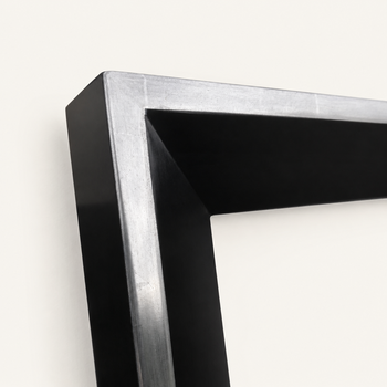 Lower corner of the 152WG profile — sloped satin black face descending toward the artwork, outer band of 6-karat white gold leaf wrapping around the frame