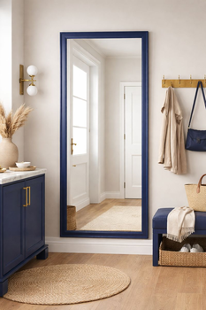 Mirror in a blue frame in a hallway setting — leaning against the wall beside a wooden console and a coat stand.