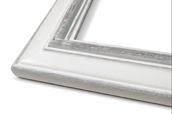 Close-up of bottom-left corner of white vintage solid wood frame – front view showing multi-level moulding profile with flat panel and carved transitions covered in heavy distressing